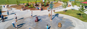Several children and caregivers enjoy the splash pad with stone water elements, splashing bear and pine tree with buckets