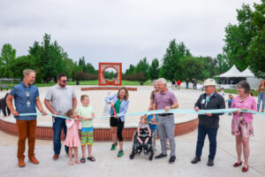 People gather around a woman cutting a ribbon with a splash pad and circular art installation in the background