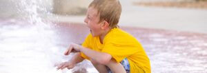 Boy reacts as he puts his hand into a ground spray at Ward County Event Center splash pad