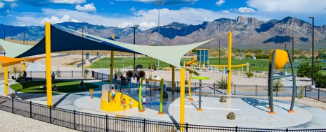 Wide shot of Naranja Park splash pad with mountains in the background and yellow posts and a light green shade structure in the foreground