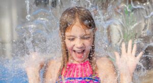 close up of a girl in a bathing suit smiling as splash pad water from above falls on her