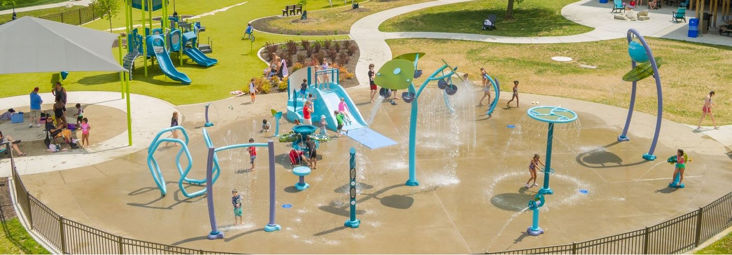 Aerial view of Aquatix splash pad with turquoise and lime green features and many kids and families playing