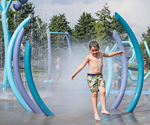A child runs through three misting arches at a splash pad