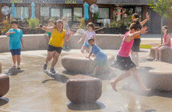 Children running with hands up amid misting ground sprays at Blue Ash Towne Square