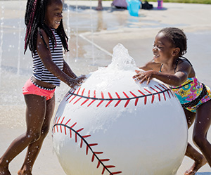 Two children play on a baseball-themed splash play feature