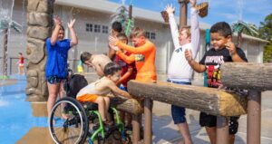A group of boys play on a set of aqualogs that flow with water on a splash pad