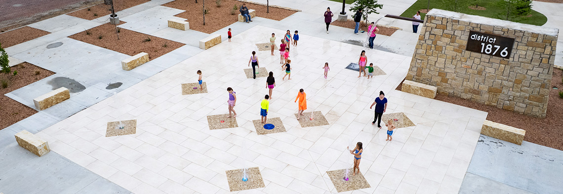 wide shot of people playing on a splash pad with ground sprays