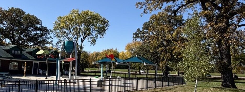 Empty splash pad in the off-season with blue dumping bucket and blue shades surrounded by trees