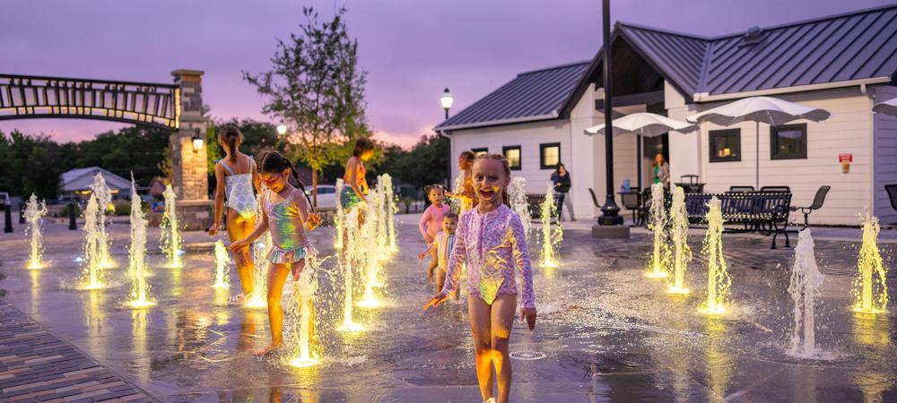 Little girl looks at camera while standing on LED lighted ground spray at splash pad